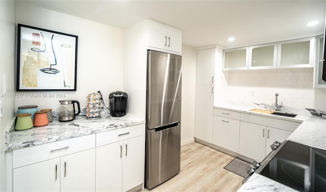 kitchen with light stone countertops, light wood-type flooring, sink, white cabinets, and stainless steel refrigerator