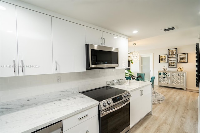 kitchen featuring white cabinets, decorative light fixtures, stainless steel appliances, and light stone countertops