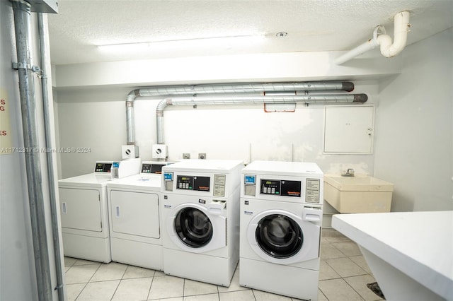 laundry area with washer and clothes dryer, light tile patterned flooring, sink, and a textured ceiling