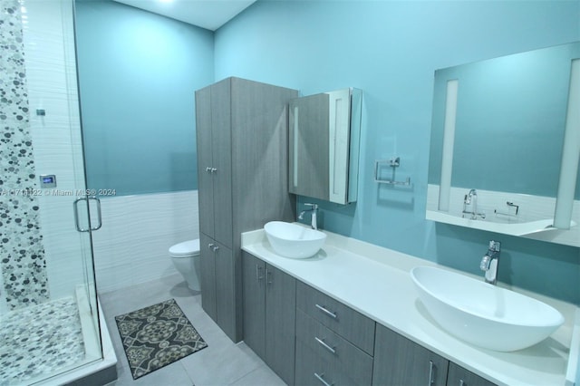 bathroom featuring tile patterned floors, toilet, vanity, a shower with shower door, and tile walls