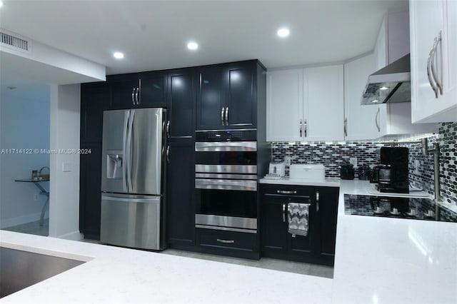 kitchen with wall chimney exhaust hood, decorative backsplash, light stone countertops, appliances with stainless steel finishes, and white cabinetry