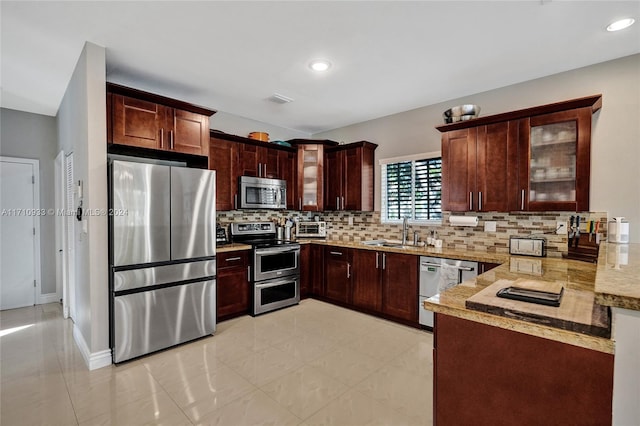 kitchen featuring kitchen peninsula, backsplash, light stone counters, stainless steel appliances, and sink