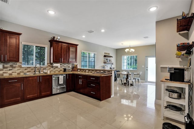 kitchen with kitchen peninsula, tasteful backsplash, sink, light tile patterned floors, and an inviting chandelier