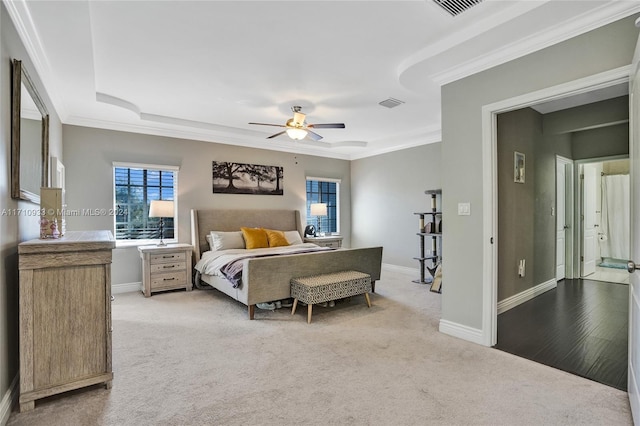 bedroom featuring ceiling fan, light colored carpet, ornamental molding, and a tray ceiling