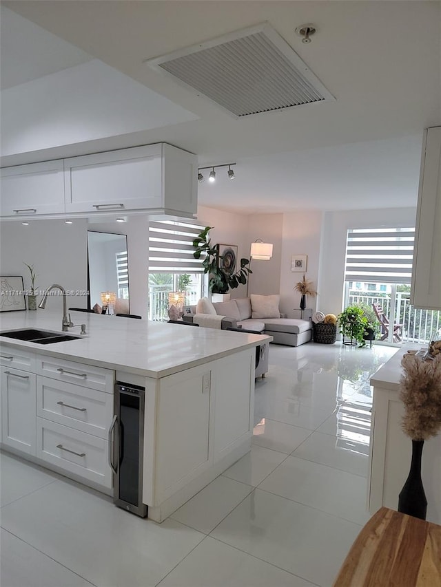 kitchen with white cabinets, light tile patterned floors, sink, and beverage cooler