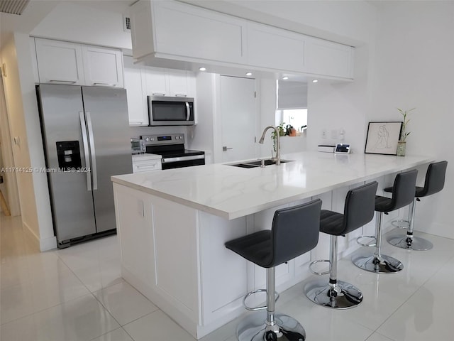 kitchen with kitchen peninsula, stainless steel appliances, sink, white cabinets, and light tile patterned flooring