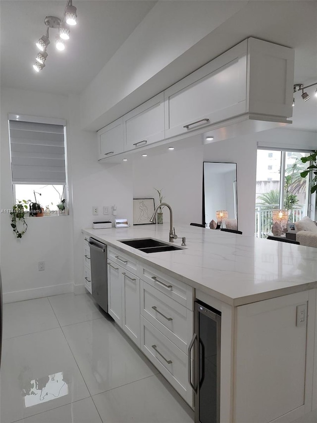 kitchen with stainless steel dishwasher, white cabinets, sink, and beverage cooler