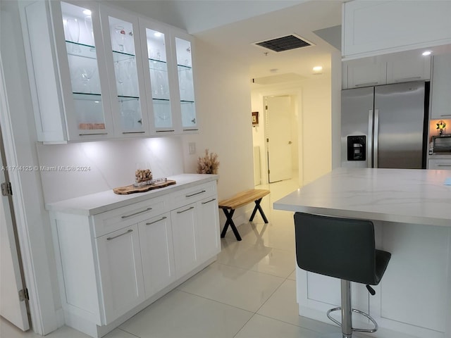 kitchen with stainless steel fridge, light stone countertops, light tile patterned floors, white cabinetry, and a breakfast bar area