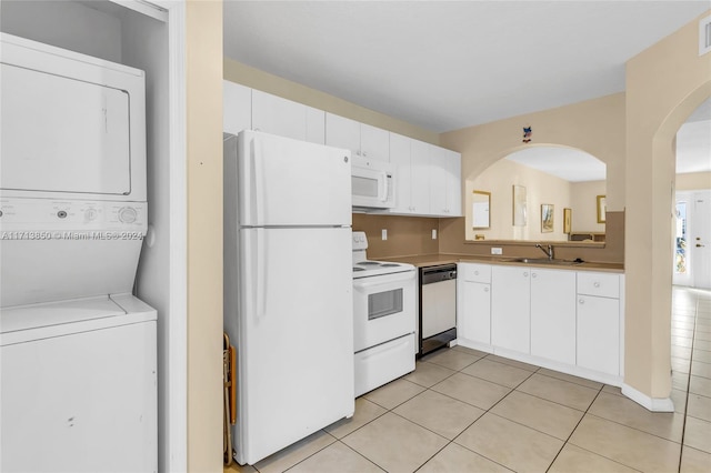 kitchen with white cabinetry, stacked washer and dryer, light tile patterned flooring, and white appliances