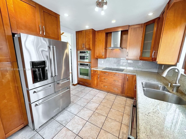 kitchen featuring sink, wall chimney range hood, light stone counters, decorative backsplash, and appliances with stainless steel finishes