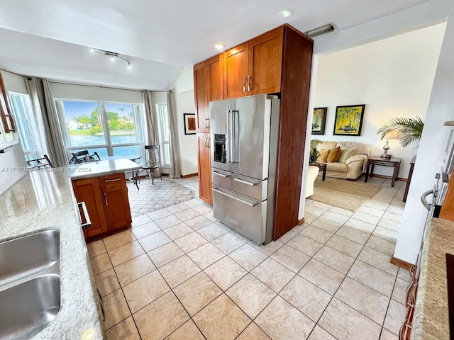 kitchen with light stone countertops, high end refrigerator, sink, light tile patterned floors, and lofted ceiling