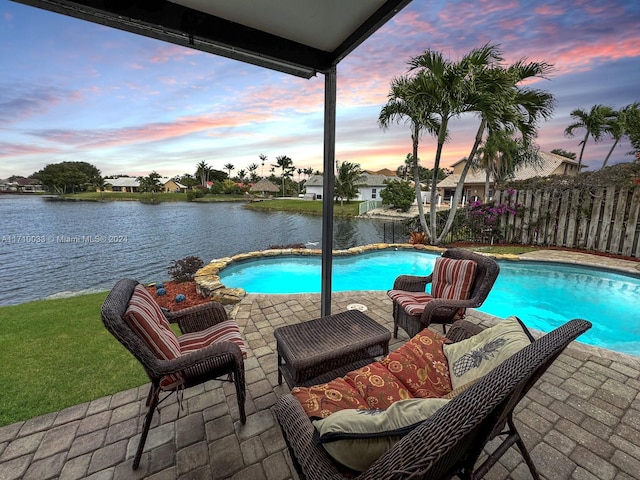 pool at dusk with a patio area and a water view