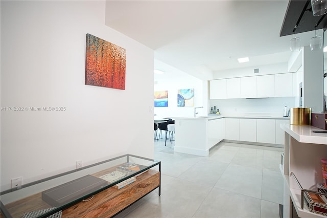 kitchen with kitchen peninsula, white cabinetry, sink, and light tile patterned floors