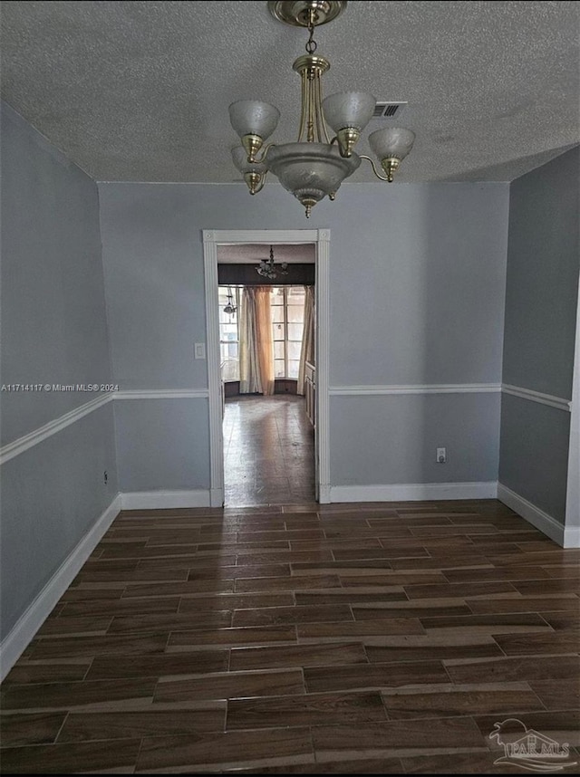 spare room with dark wood-type flooring, a textured ceiling, and an inviting chandelier