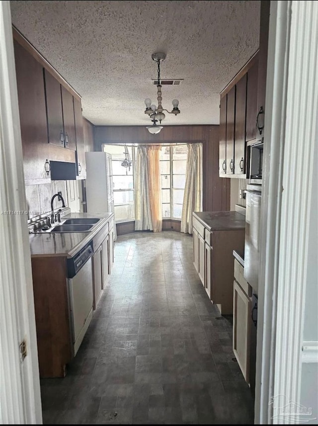 kitchen with a textured ceiling, sink, a notable chandelier, dishwasher, and wood walls