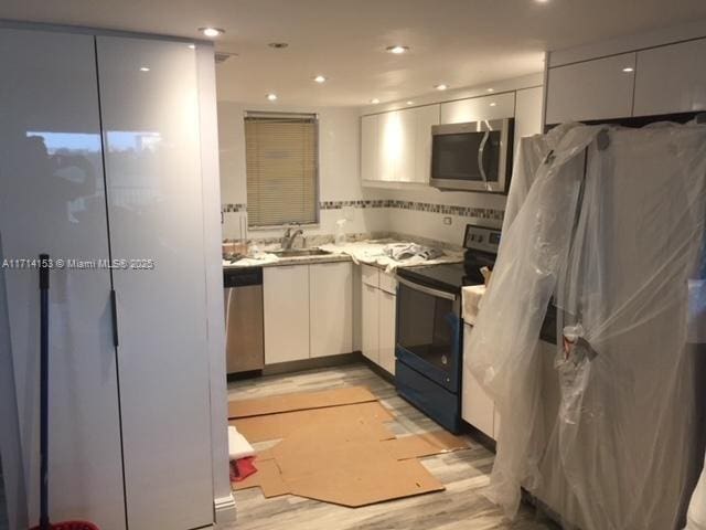 kitchen featuring white cabinetry, sink, light hardwood / wood-style floors, and appliances with stainless steel finishes