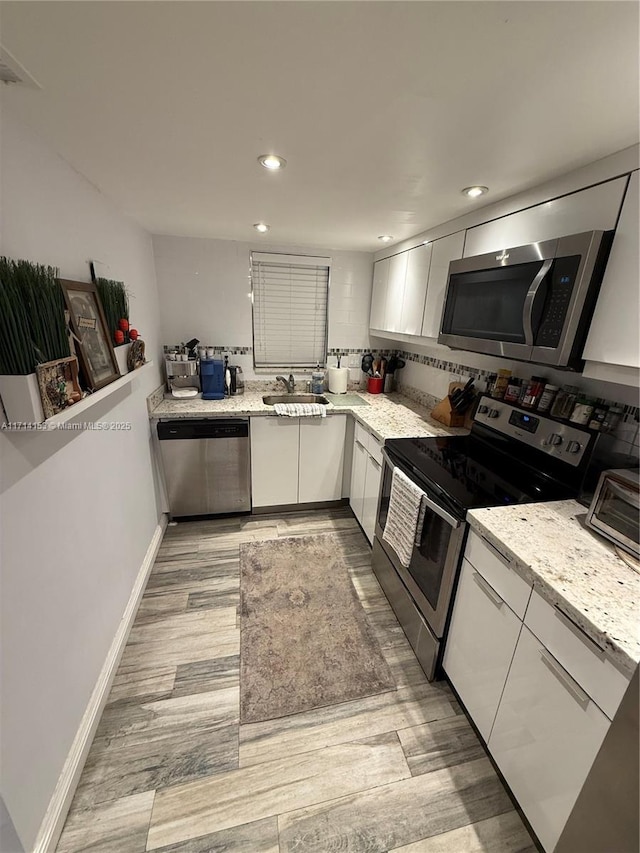 kitchen with light stone counters, white cabinetry, light wood-style floors, stainless steel appliances, and a sink