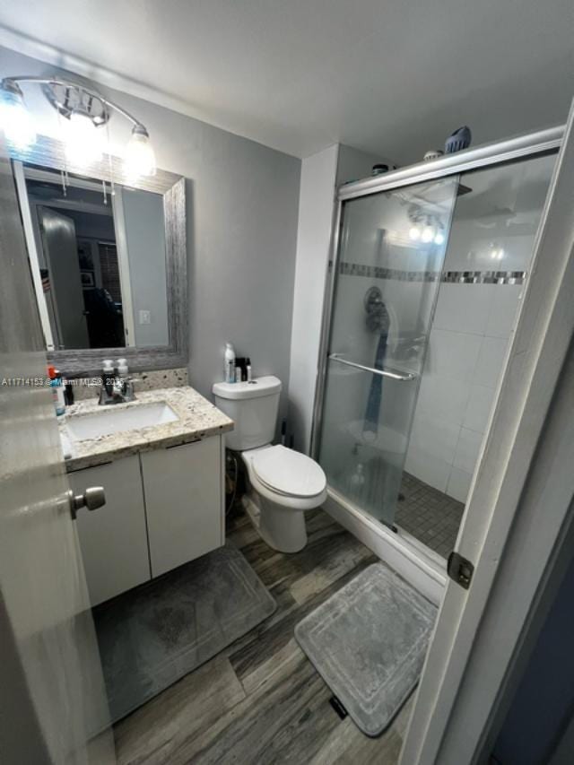 bathroom with walk in shower, vanity, wood-type flooring, and toilet