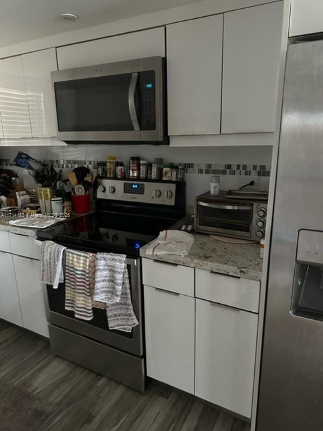 kitchen with light stone countertops, appliances with stainless steel finishes, tasteful backsplash, dark hardwood / wood-style floors, and white cabinetry