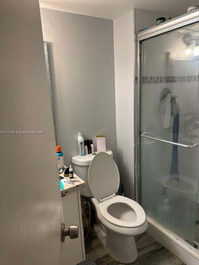 bathroom with wood-type flooring, vanity, toilet, and a shower with shower door