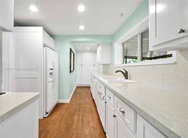 kitchen with light stone countertops, sink, hardwood / wood-style flooring, white cabinetry, and white fridge with ice dispenser