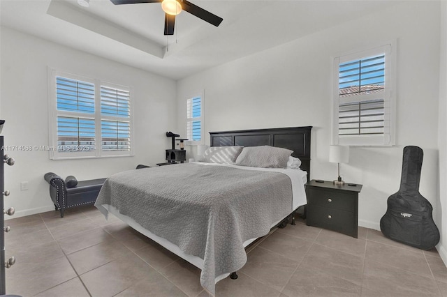 bedroom featuring multiple windows, light tile patterned flooring, ceiling fan, and a tray ceiling