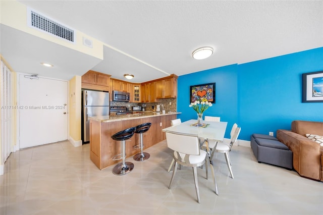 kitchen featuring backsplash, a breakfast bar area, light tile patterned floors, and appliances with stainless steel finishes