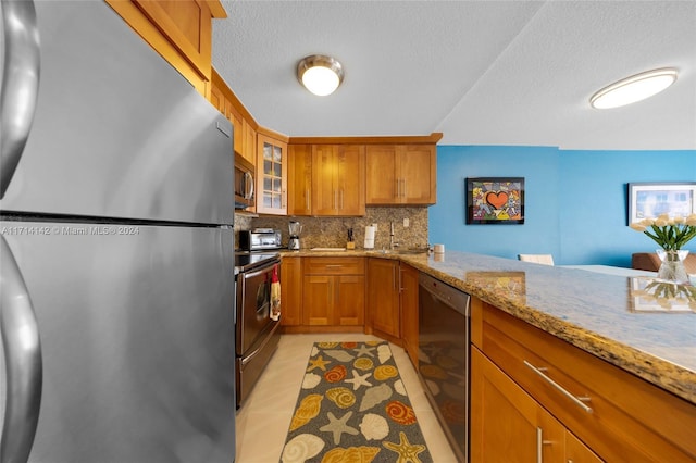 kitchen with decorative backsplash, light stone countertops, light tile patterned floors, kitchen peninsula, and stainless steel appliances