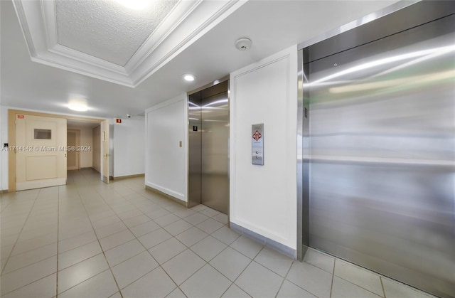 hall featuring a textured ceiling, elevator, a raised ceiling, and ornamental molding