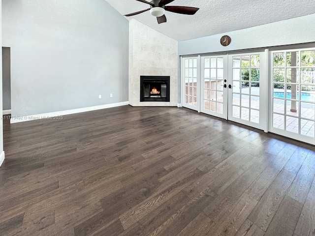 unfurnished living room with dark wood-type flooring, french doors, lofted ceiling, a textured ceiling, and a tile fireplace