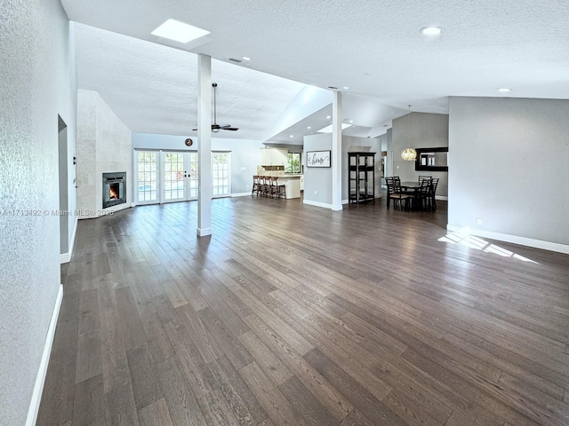 unfurnished living room featuring vaulted ceiling, dark hardwood / wood-style floors, a fireplace, and a textured ceiling