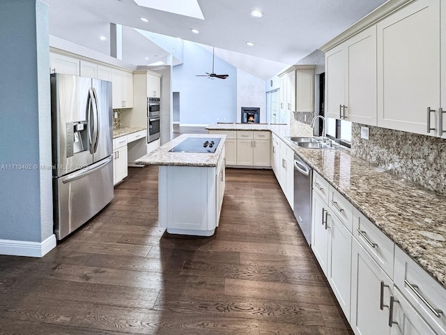 kitchen with sink, appliances with stainless steel finishes, lofted ceiling with skylight, tasteful backsplash, and a kitchen island