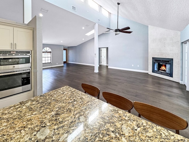 kitchen featuring dark wood-type flooring, a tile fireplace, ceiling fan, a textured ceiling, and stone countertops