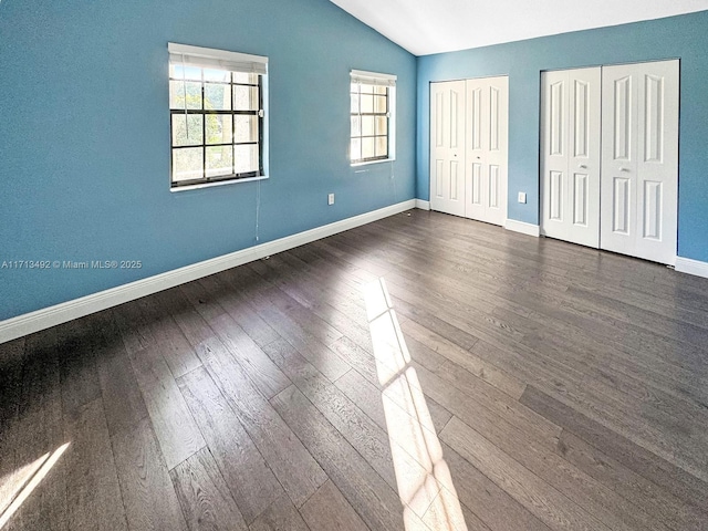 unfurnished bedroom featuring multiple windows, lofted ceiling, dark hardwood / wood-style floors, and two closets