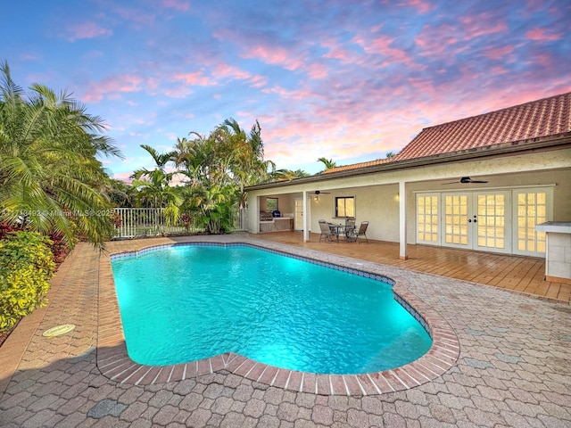 pool at dusk featuring a patio, ceiling fan, and french doors