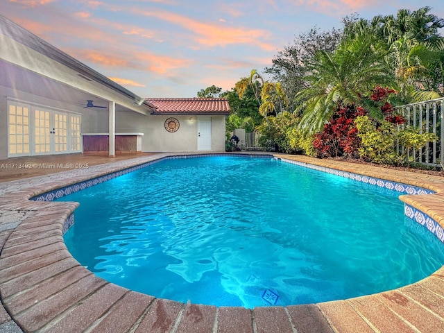 pool at dusk featuring ceiling fan and french doors