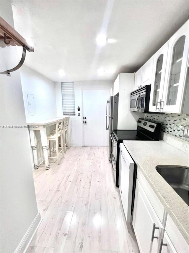 kitchen featuring backsplash, sink, light wood-type flooring, appliances with stainless steel finishes, and white cabinetry