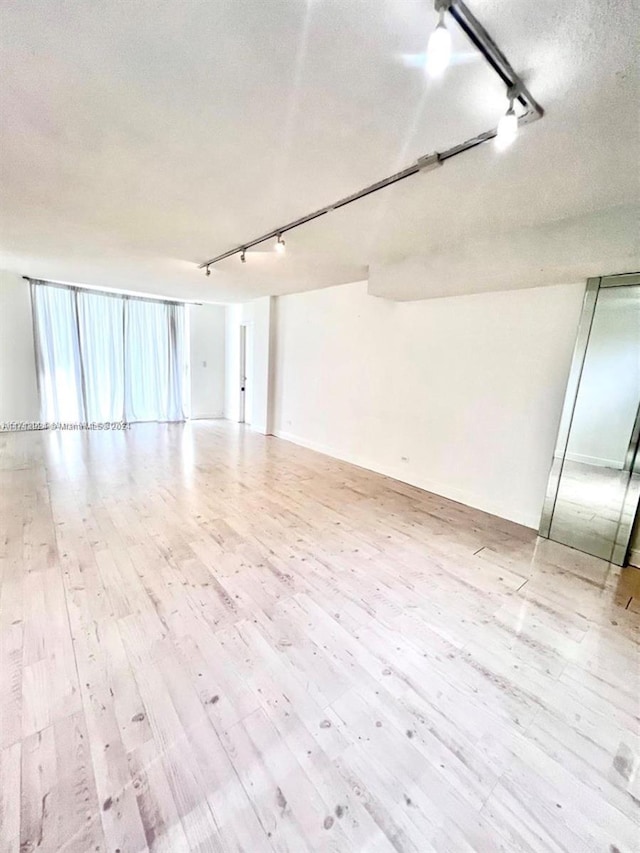 empty room featuring a textured ceiling, light hardwood / wood-style floors, a wall of windows, and rail lighting