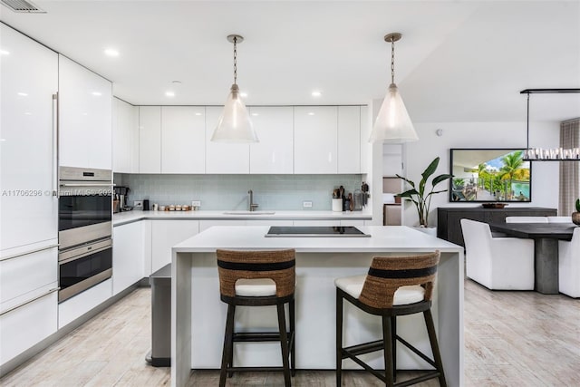 kitchen featuring black electric stovetop, decorative light fixtures, white cabinetry, and sink