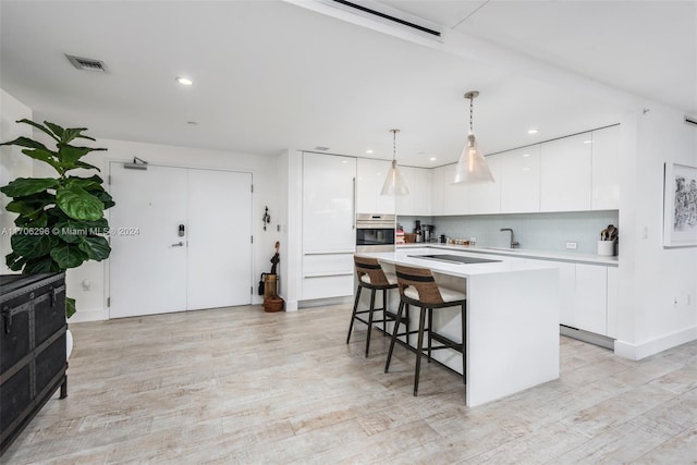 kitchen featuring white cabinetry, hanging light fixtures, tasteful backsplash, oven, and a center island with sink