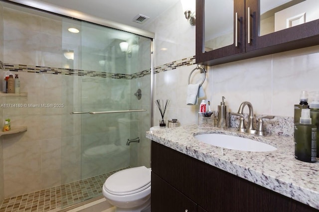 bathroom with tile walls, visible vents, toilet, a stall shower, and vanity