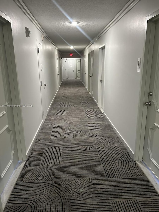 hallway featuring a textured ceiling, ornamental molding, and dark carpet