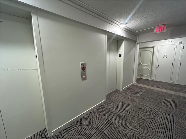 hall featuring a textured ceiling, dark carpet, and baseboards