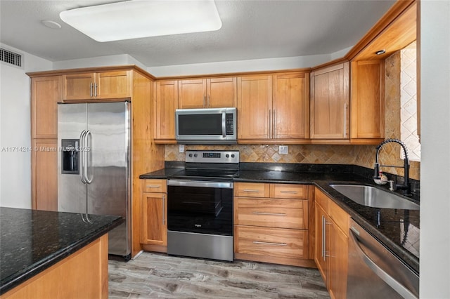 kitchen with sink, stainless steel appliances, dark stone counters, light hardwood / wood-style floors, and decorative backsplash