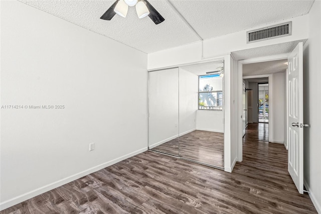 unfurnished bedroom featuring a textured ceiling, ceiling fan, dark wood-type flooring, and a closet