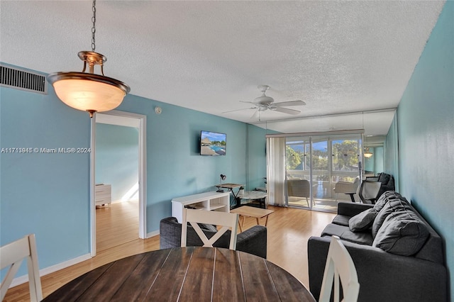 living room featuring light wood-type flooring, ceiling fan, and a textured ceiling