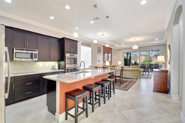 kitchen featuring a breakfast bar, a kitchen island with sink, hanging light fixtures, sink, and appliances with stainless steel finishes