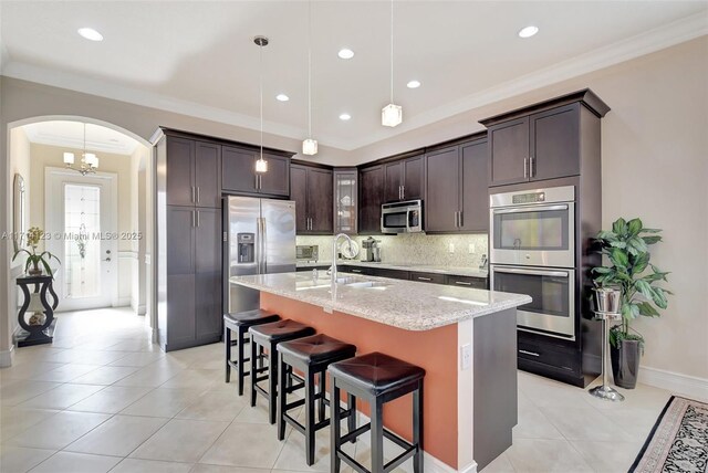 kitchen with sink, light stone counters, a center island with sink, dark brown cabinets, and appliances with stainless steel finishes