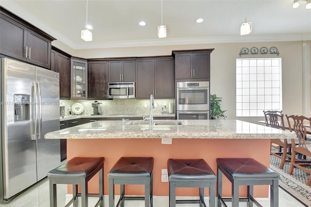 kitchen with a center island with sink, sink, ornamental molding, appliances with stainless steel finishes, and decorative light fixtures