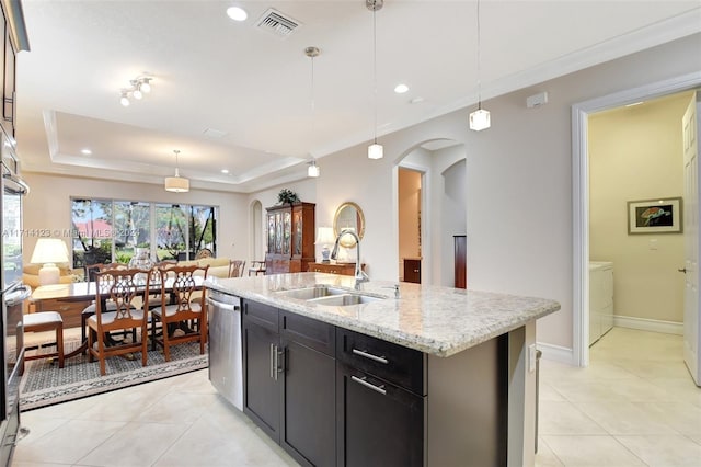 kitchen featuring a tray ceiling, dishwasher, a center island with sink, and decorative light fixtures